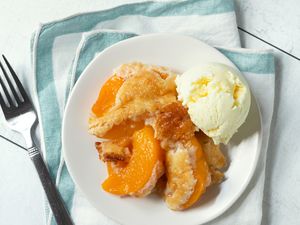 Peach cobbler served on a plate with a scoop of ice cream accompanied by a fork