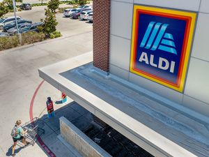 An Aldi store entrance with a shopper pushing a cart toward it