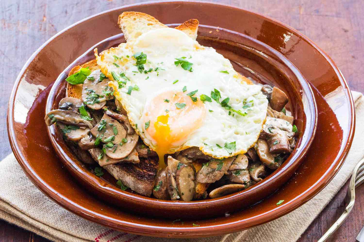 fried egg on mushroom toast on a brown plate