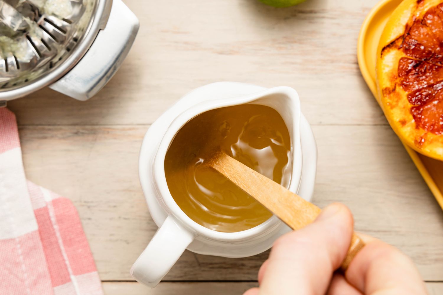 Lime-Vodka-Agave Mixed Together Using a Wooden Spoon in a Pitcher, and in the Surroundings, a Tabletop Juicer, a Tray of Grilled Grapefruit, and a Kitchen Towel