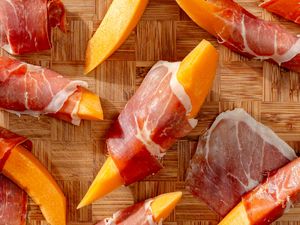 Prosciutto wrapped around melon wedges on a wooden board