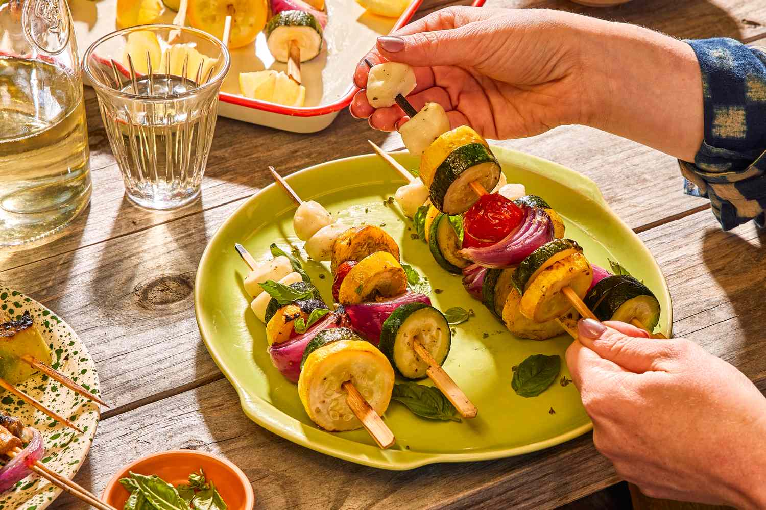 Hands assembling vegetable skewers, colorful vegetables on skewers on a plate on a rustic wooden table