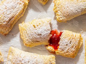 Toast Pies on a piece of parchment, dusted with powdered sugar, one torn open to show red filling