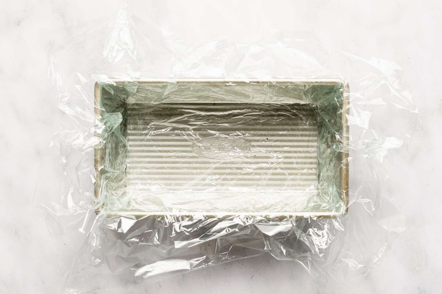 Overhead view of a metal bread baking pan with plastic wrap lining the inside for Easy British Summer Pudding recipe
