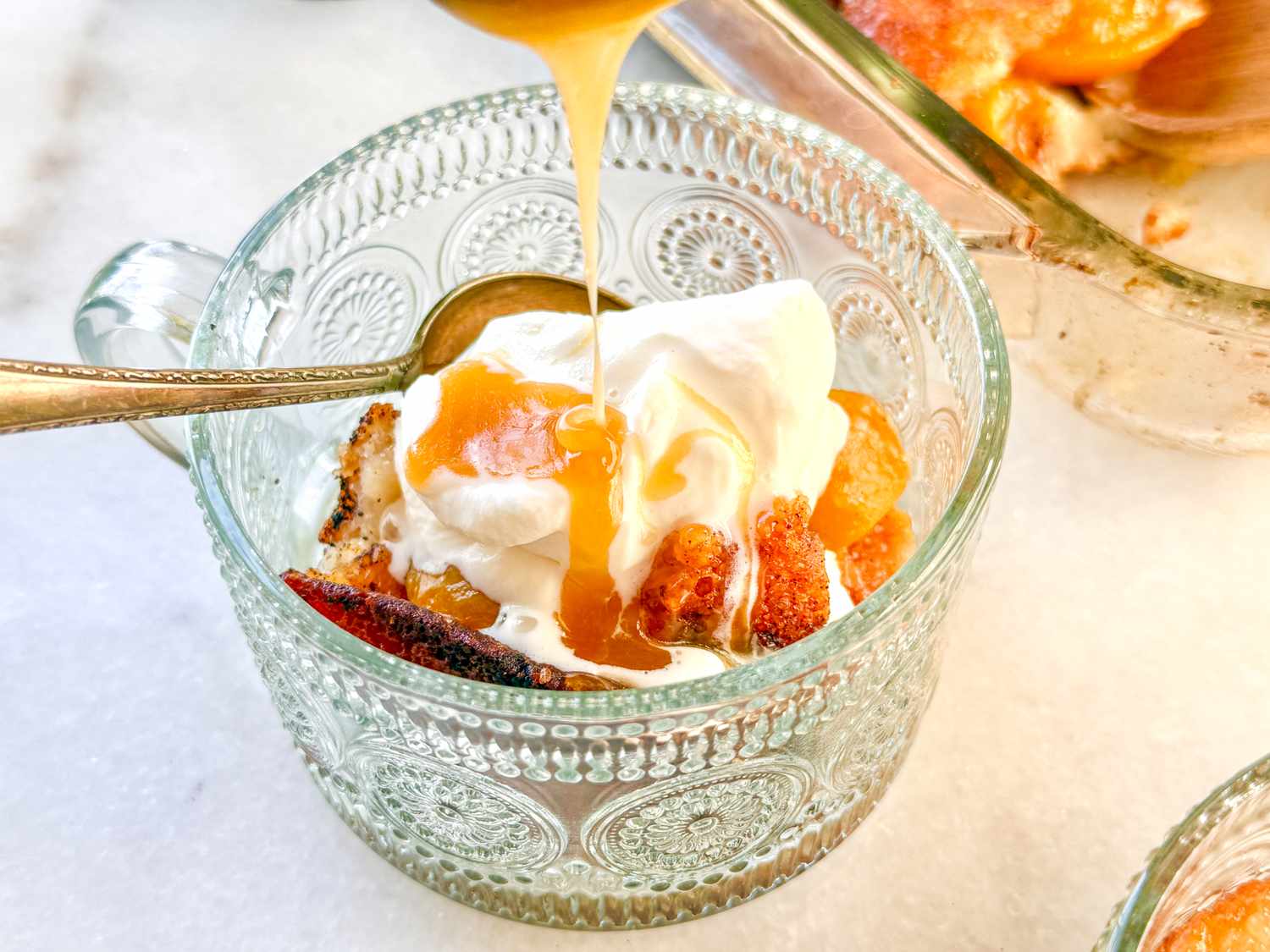 Peach cobbler dessert being prepared with cream and sauce in a glass dish
