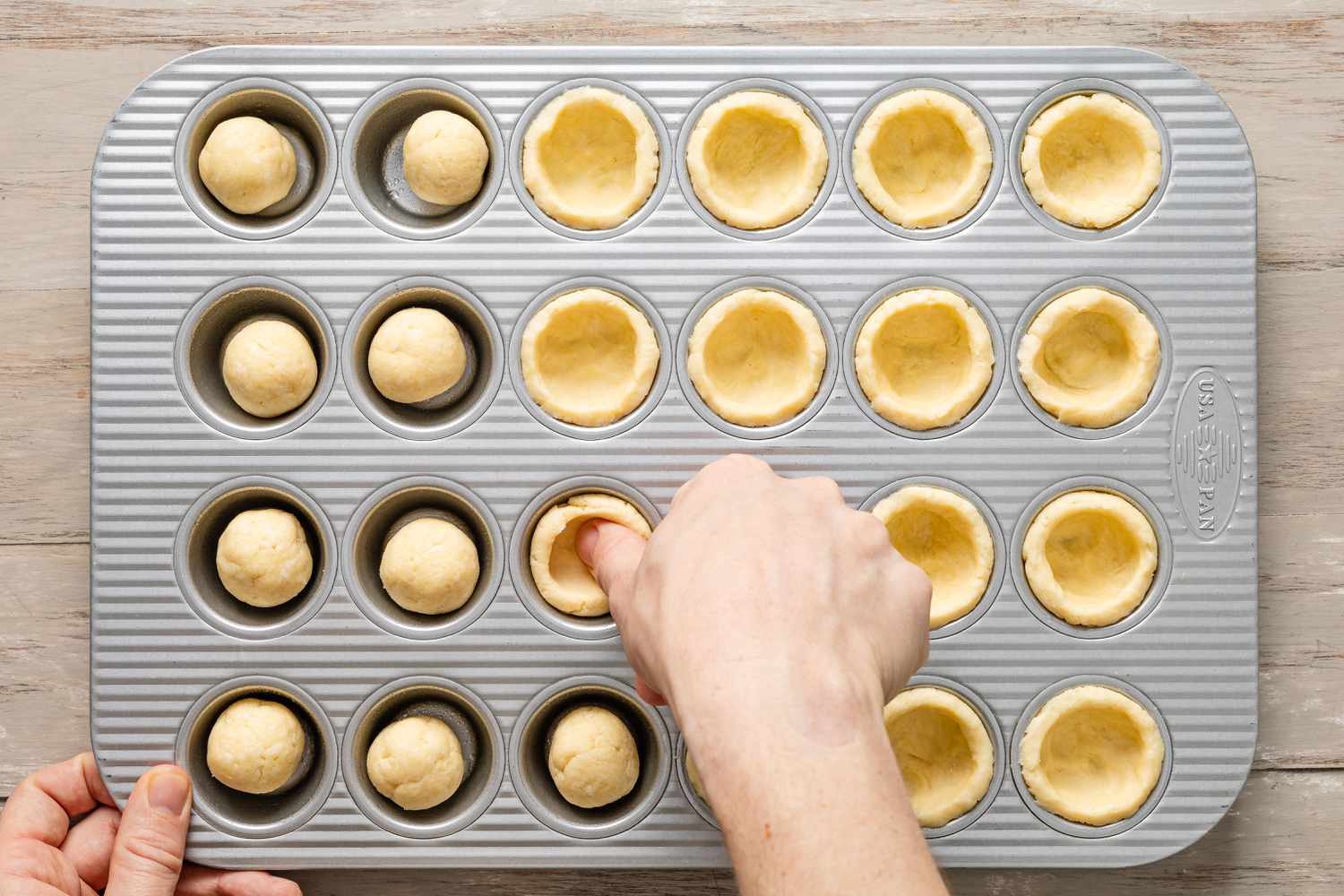 Thub flattening pecan pie cookie dough portions into the muffin pan 