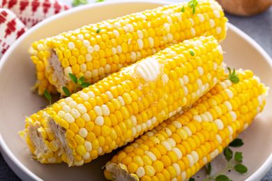 A plate with several ears of buttered corn garnished with herbs