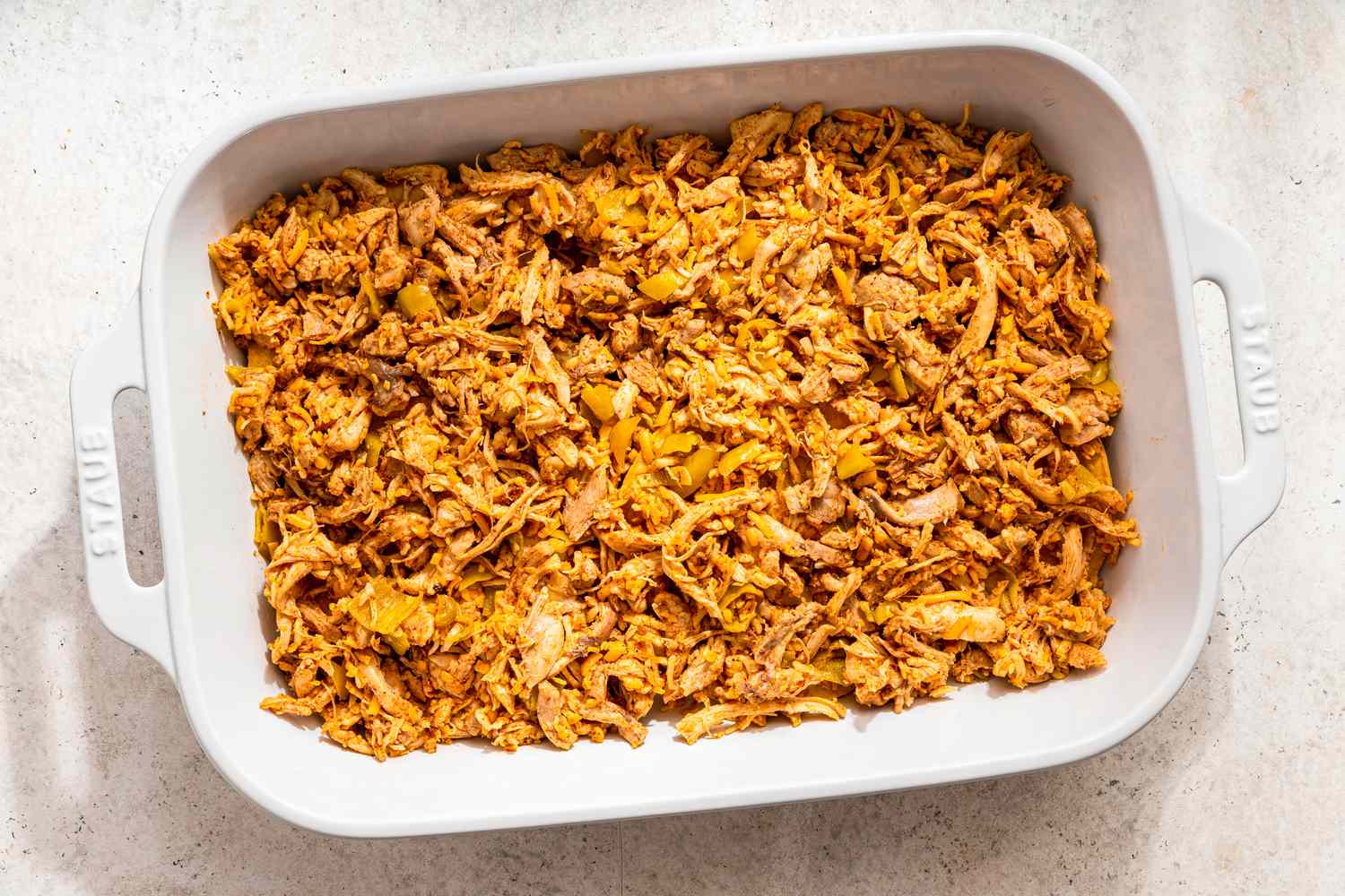 Assembling chicken taco casserole: shredded chicken added on top of the tostada layer 
