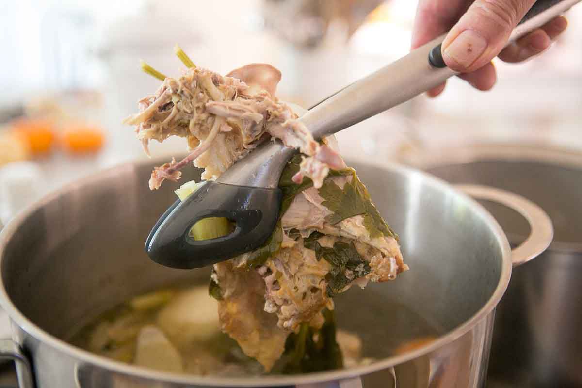 Tongs pulling a turkey carcass out of a pot