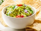 Fresh guacamole in a small white bowl with tortilla chips surrounding it