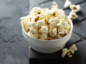 Bowl of popcorn with pieces scattered nearby on a dark textured surface