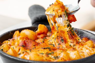 Pasta dish topped with melted cheese being pulled with a fork