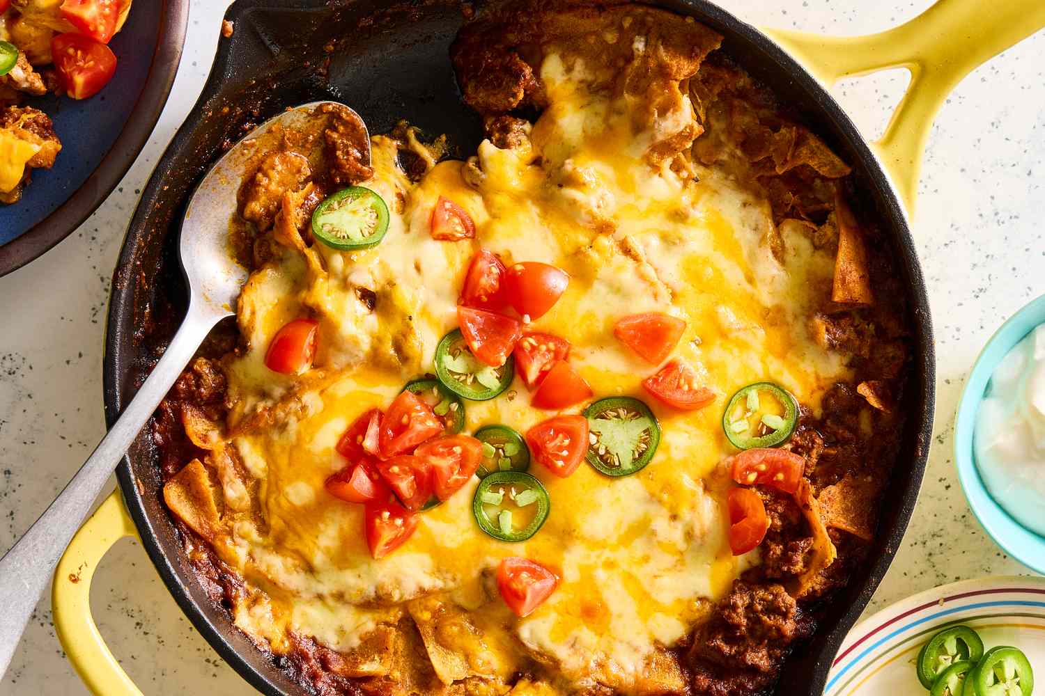 Beef enchilada skillet topped with melted cheese, sliced jalapeños, and diced tomatoes