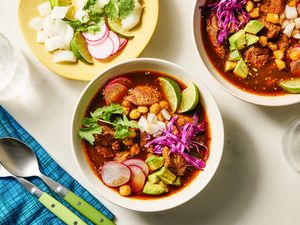 Pozole rojo served in two bowls with garnishes on a plate and a blue napkin nearby