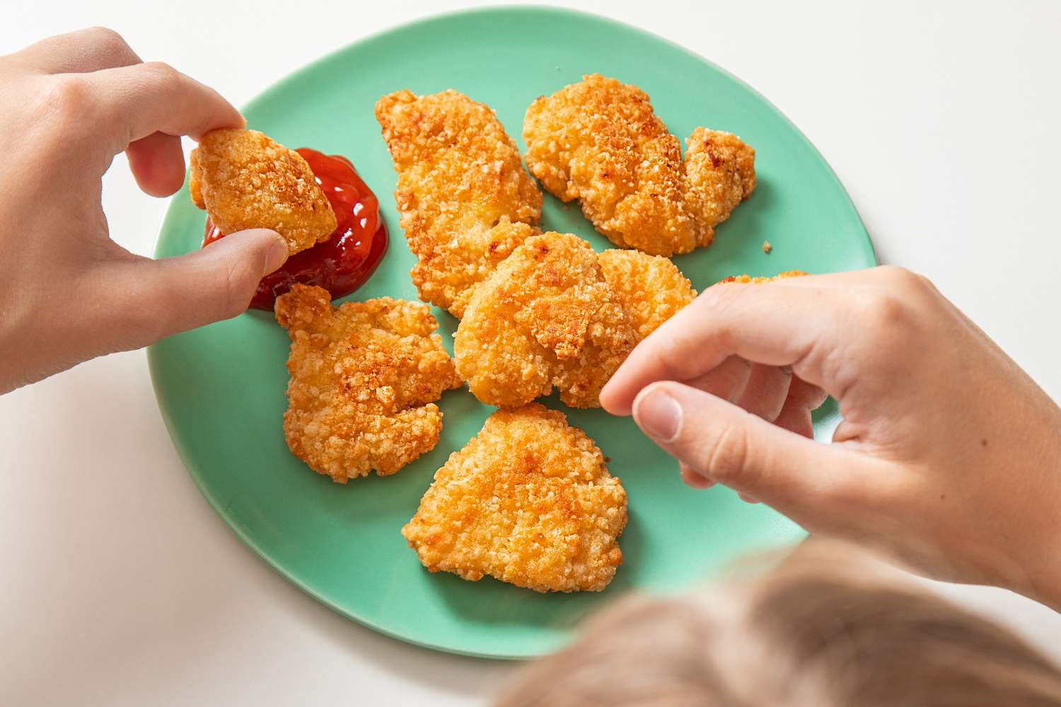 Hands over a green plate with Trader Joe's chicken nuggets and ketchup