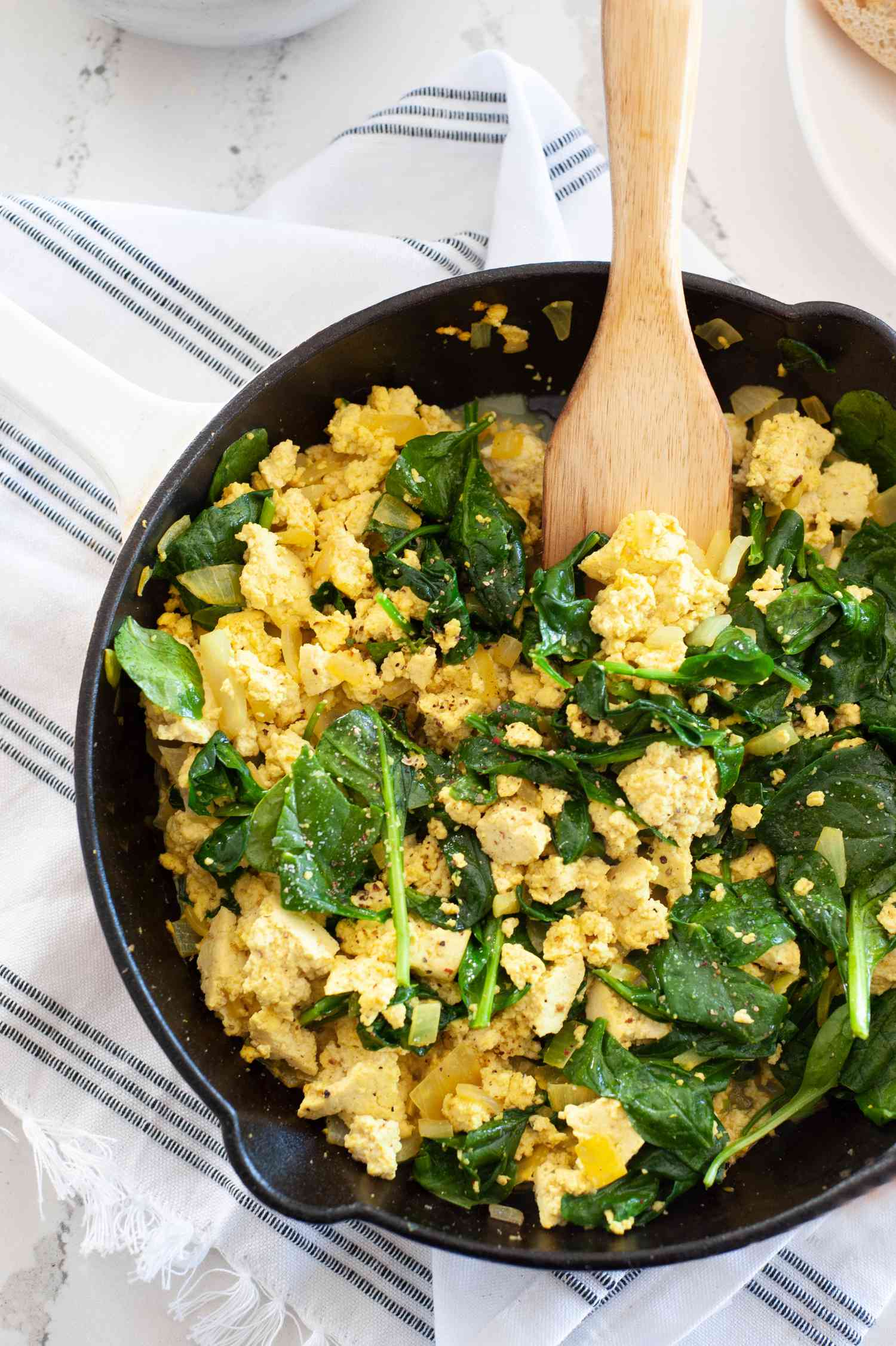 Easy spinach tofu scramble in skillet with wooden spoon.