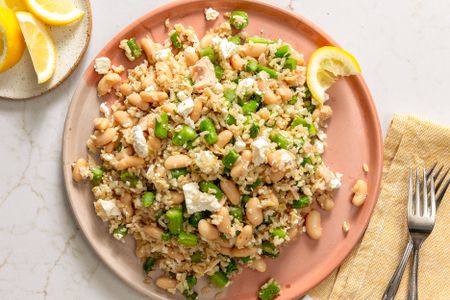 Plated asparagus and brown rice dish with beans and garnishes on a light surface with cutlery and a lemon wedge nearby