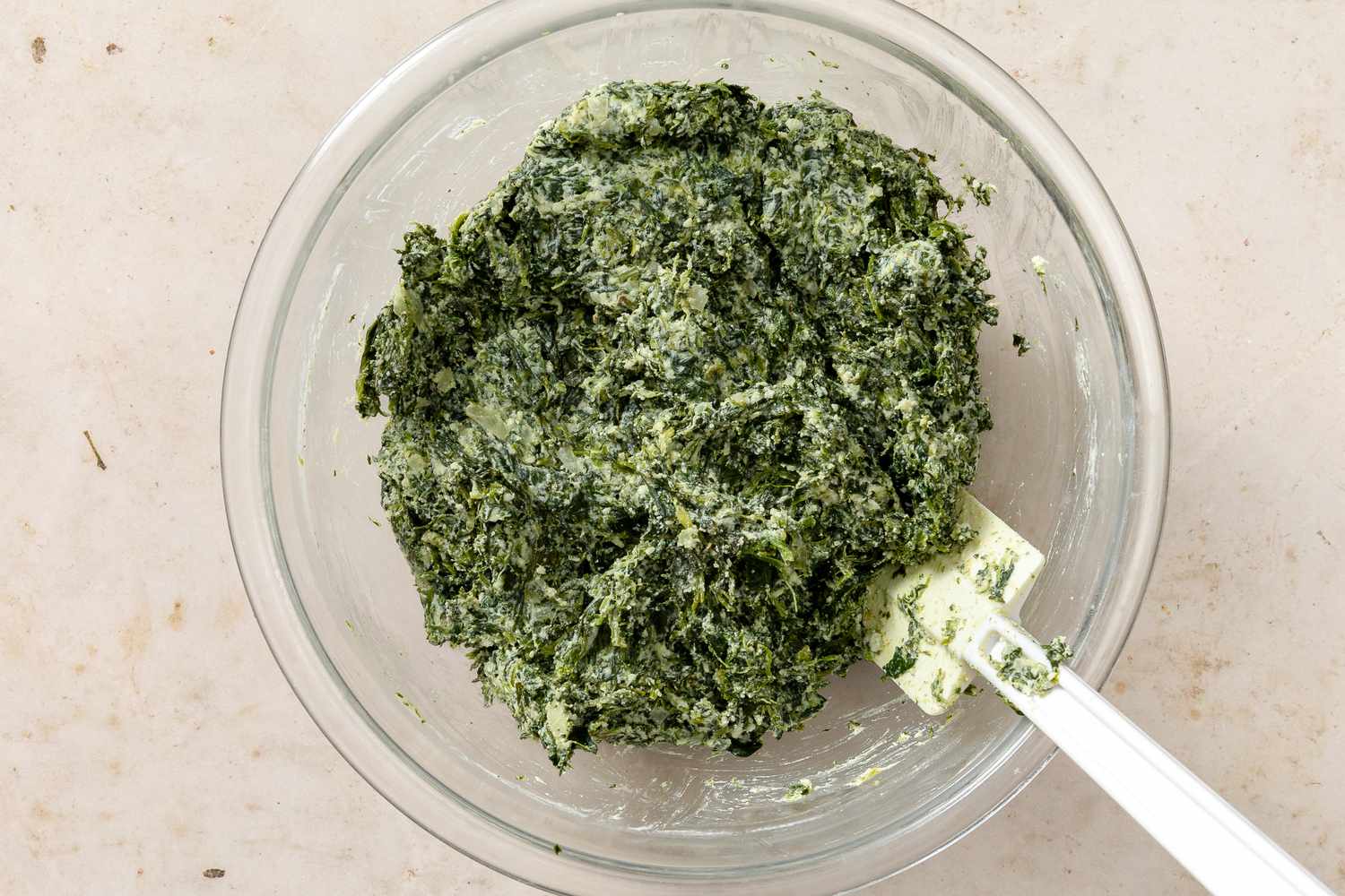 Overhead view of a clear glass mixing bowl of the ricotta mixture mixed for Ravioli Gnudi Recipe
