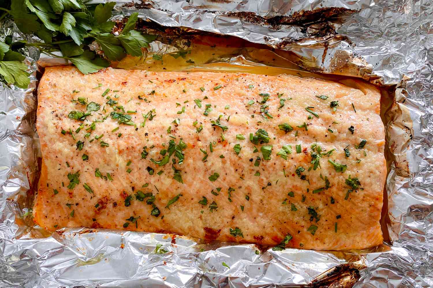 A honey and garlic butter roasted salmon topped with herbs and resting on foil