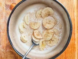 A bowl containing sliced bananas in milk with a sprinkle of cinnamon and a spoon