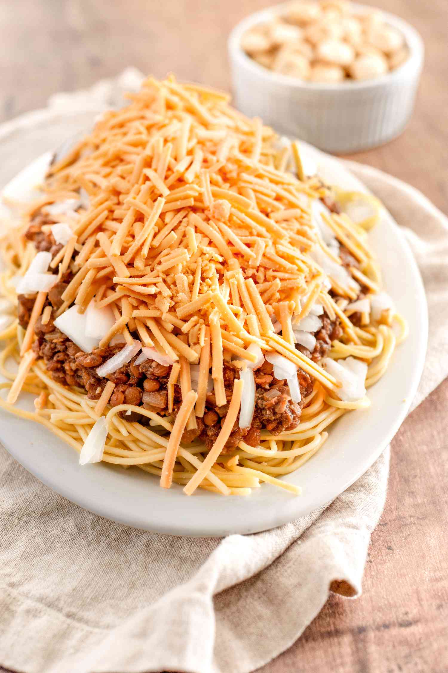 Vegan Cincinnati Chili Served over a Platter of Pasta and Topped with Cheese and Onions