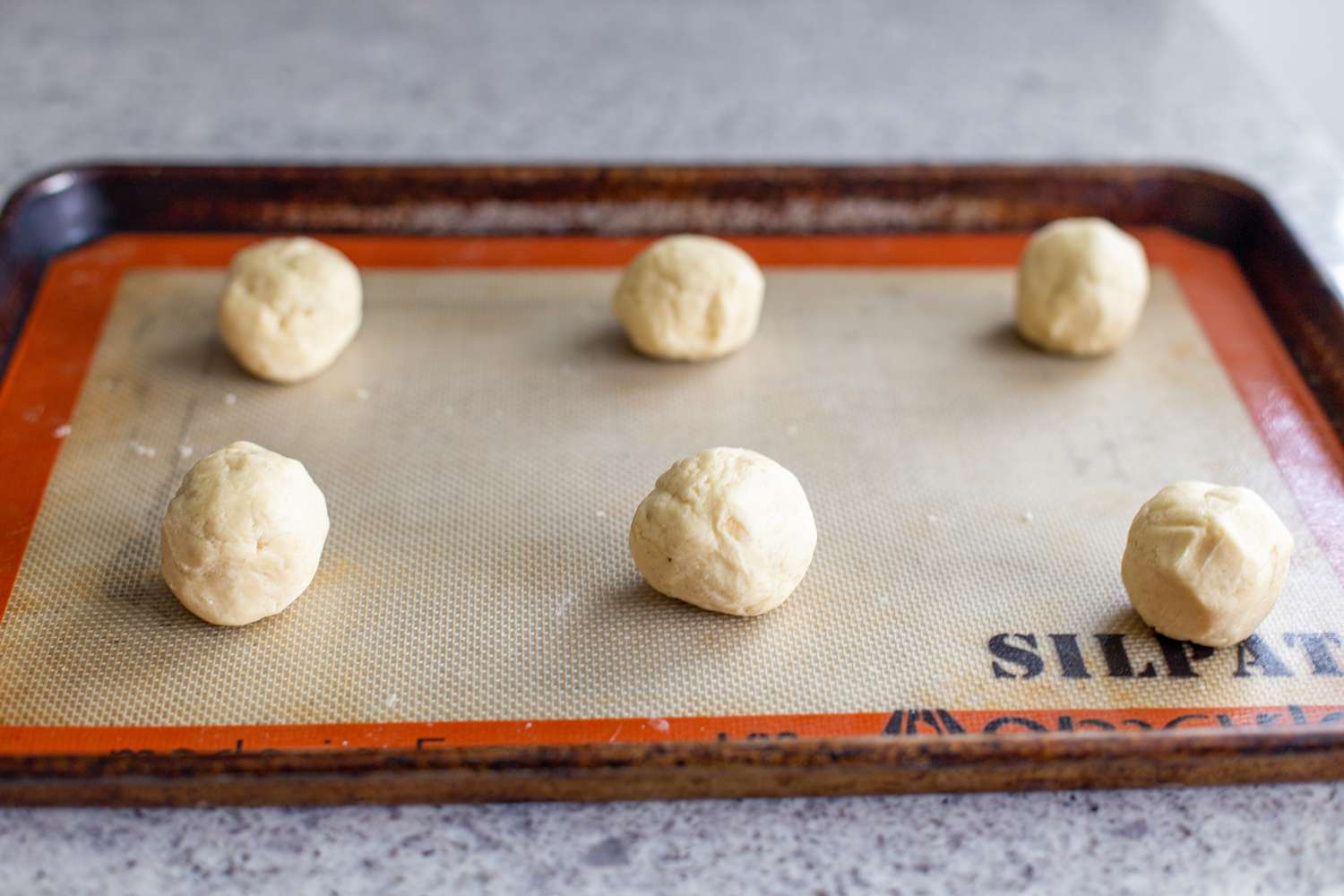 Almond-flavored butter cookie dough in balls on a baking sheet.