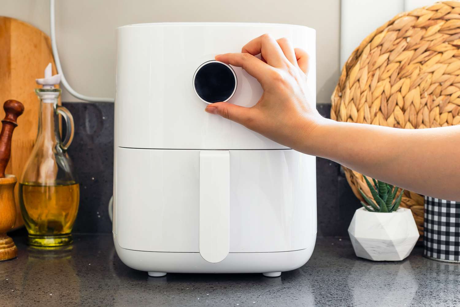 An air fryer on a kitchen counter with a hand reaching in to adjust the dial