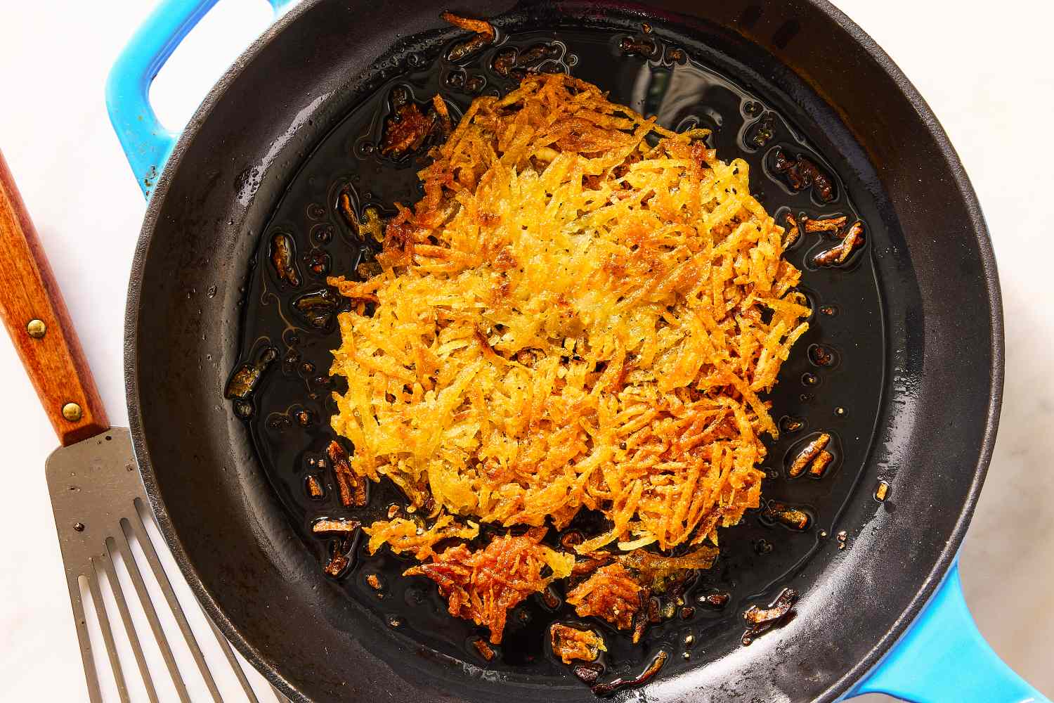 A pan with crispy hash browns being cooked a spatula on the side