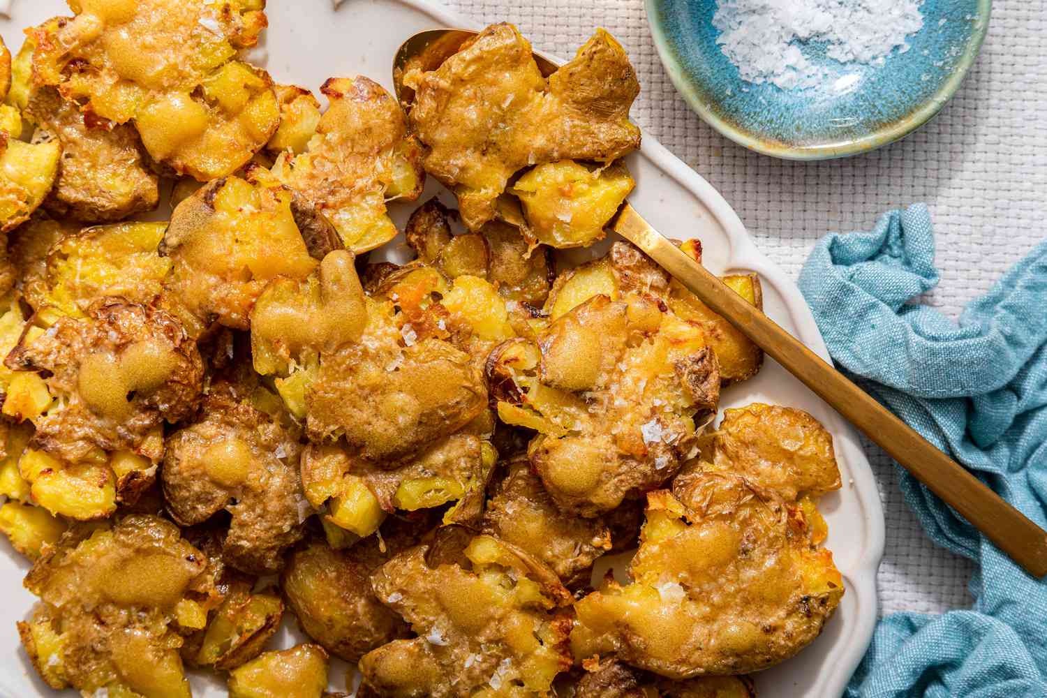 Crash hot potatoes on a platter next to a small saucer with flaky salt and a kitchen towel