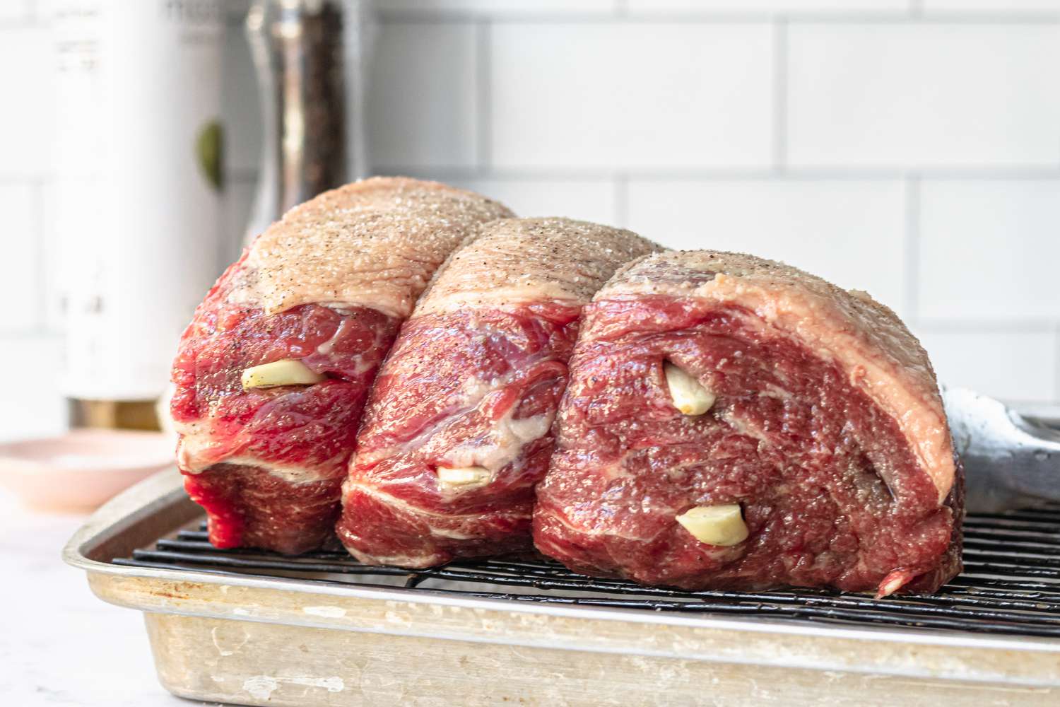 Side view of a baking tray with a rump roast set on a rack with garlic cloves pressed into it