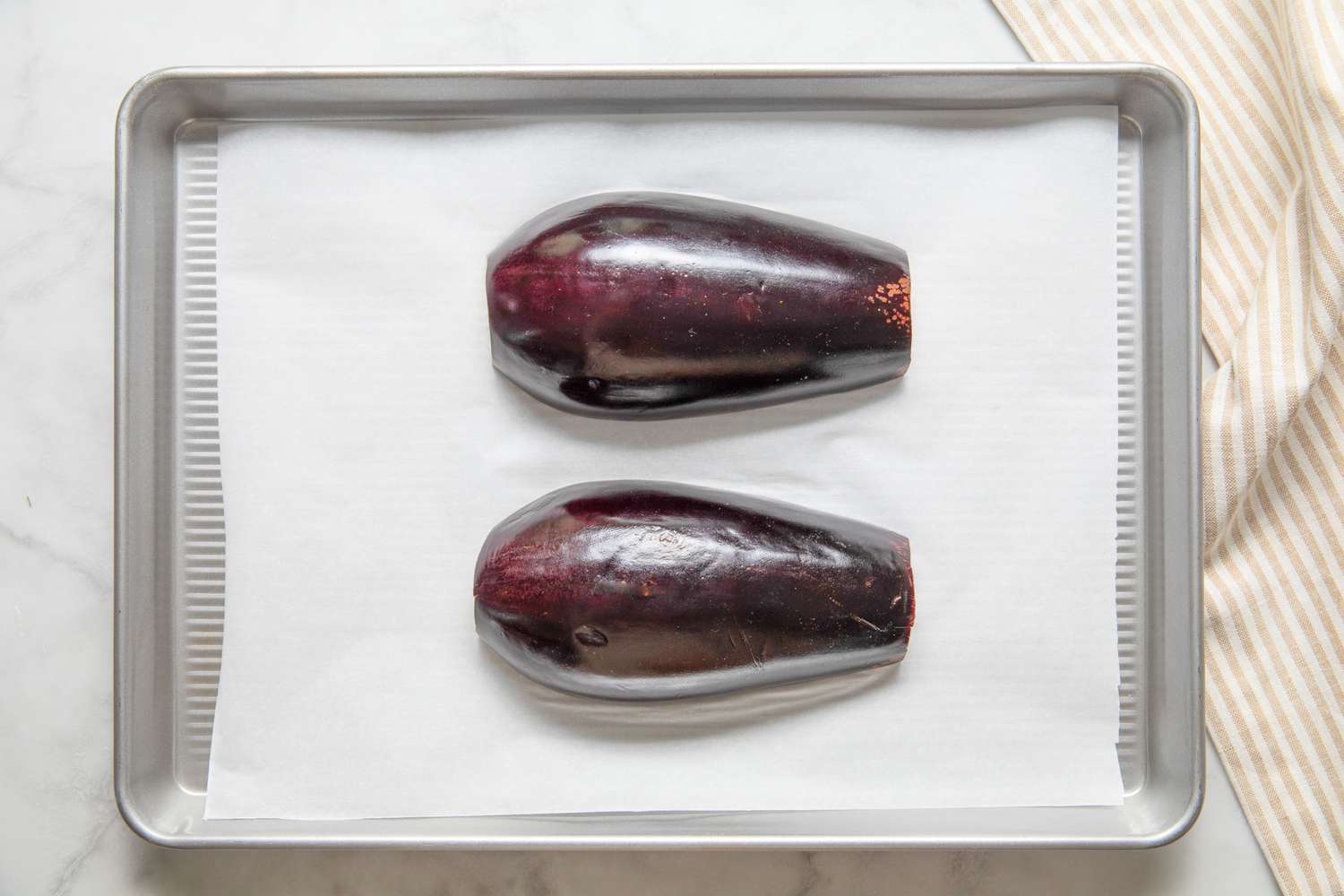 Halved Eggplant Placed on a Parchment Lined Baking Tray, Score Side Down