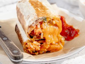 Easy Rice and Beans Freezer Burritos Stacked Together on a Plate With a Table Knife and Salsa 