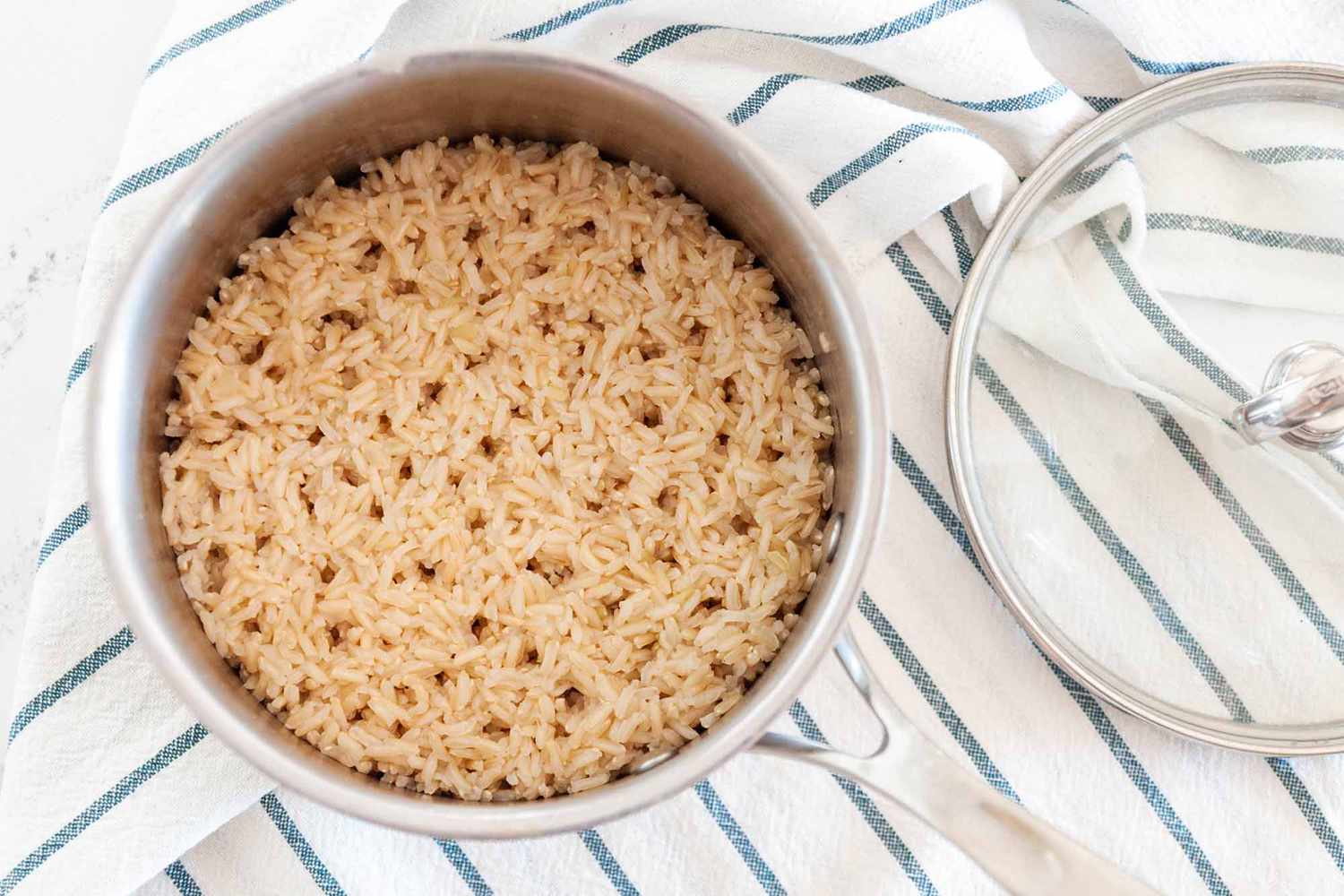 Overhead of brown rice in a pot with a lid to the side