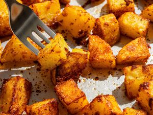 Cubed roasted potatoes with dark-spiced char, a fork lifting one piece