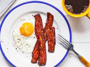 Over easy eggs on a blue rimmed plate with a side of bacon.