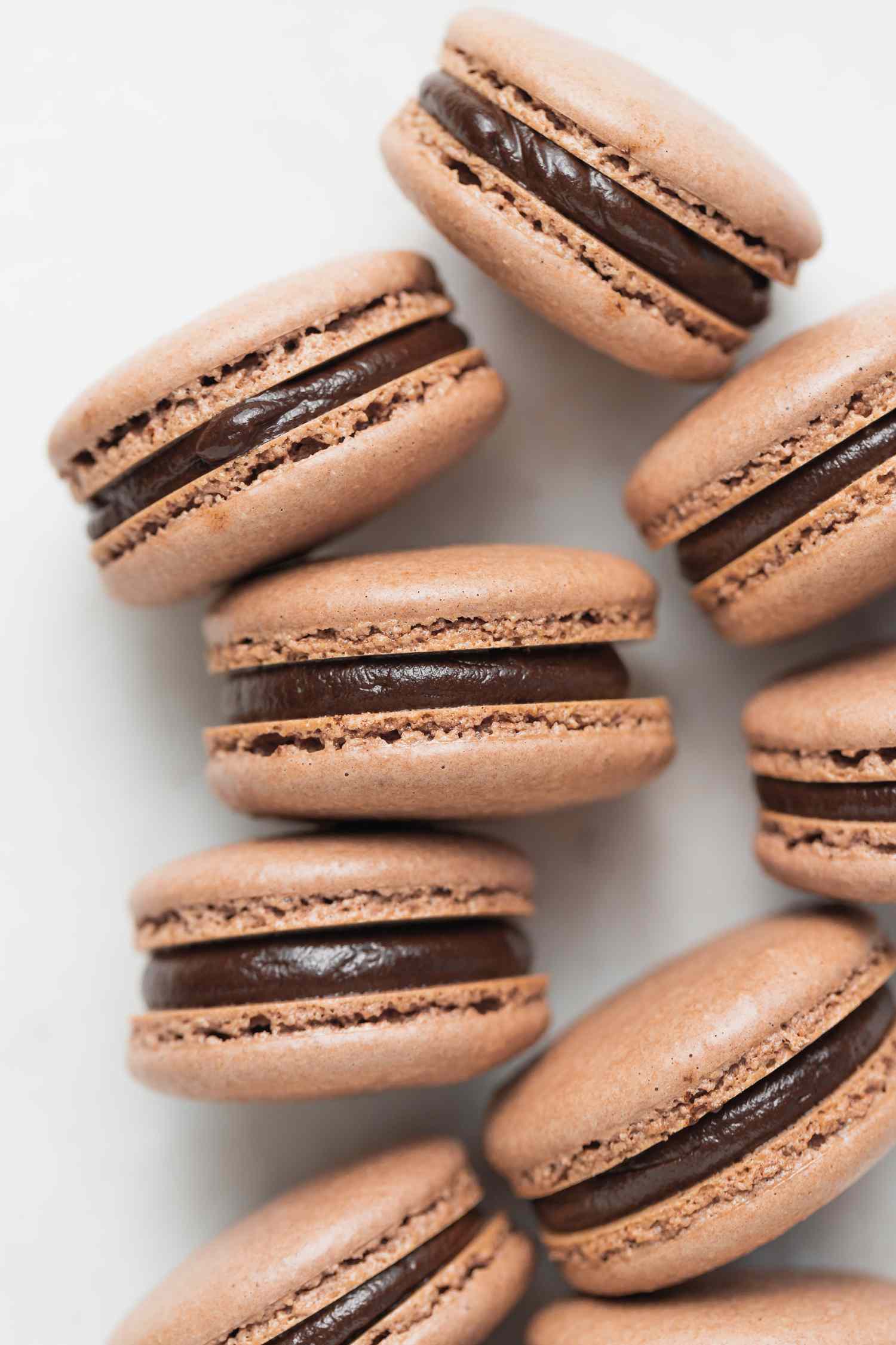 Dark chocolate ganache-filled macarons set on a white background on their side.