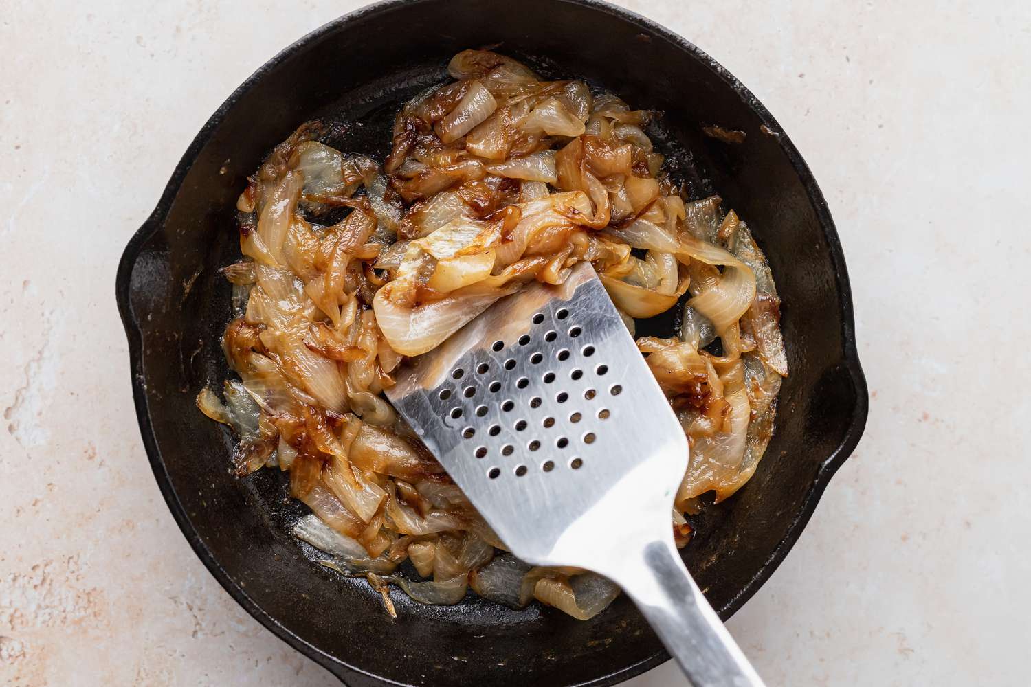 A metal spatula stirring sautéd onions in a cast iron skillet