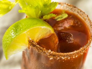 A closeup of a salt-rimmed glass with bloody Mary, garnished with a lime wedge and lime wedge