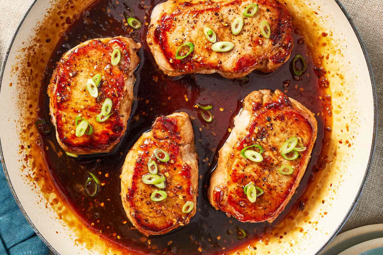 Cooked pork chops garnished with sliced green onions in a pan of sauce