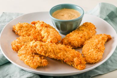 Angled view of a white plate of air fryer potato chip chicken tenders along with a small bowl of dipping sauce