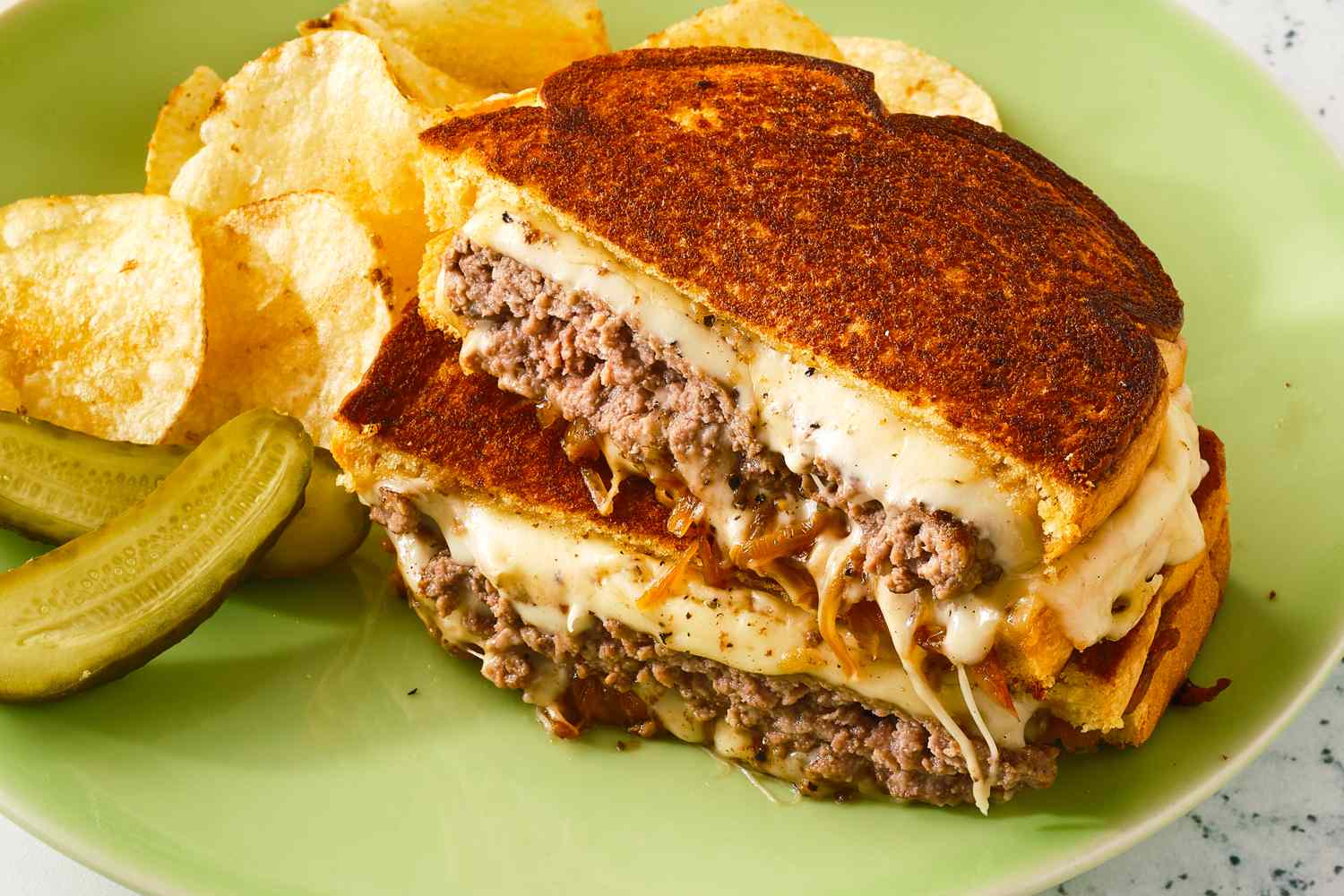 Patty melt sandwich with chips and pickles on a plate