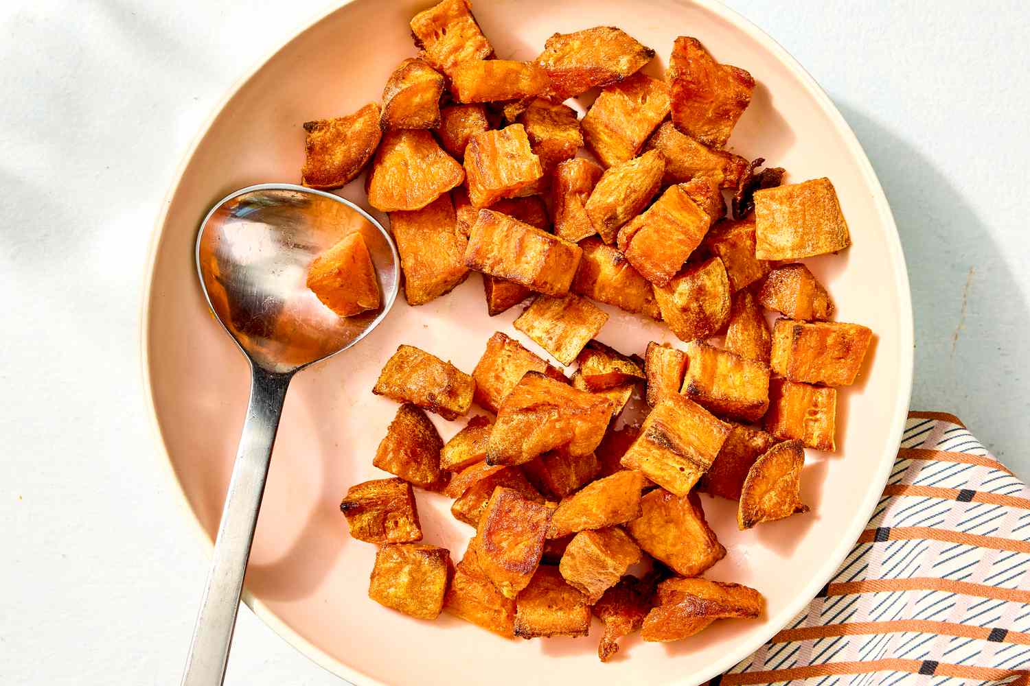 Overhead view of a bowl with cubes of roasted sweet potato along with a metal spoon