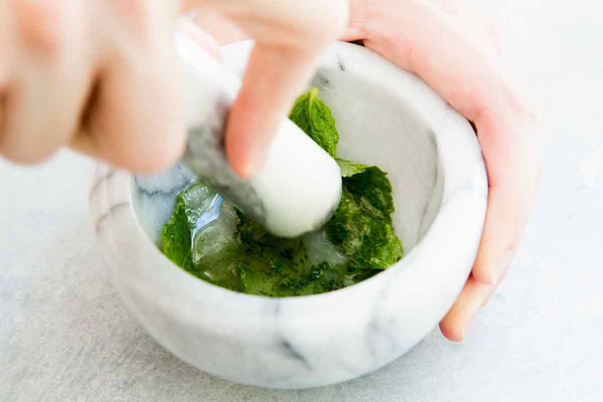 Mash the mint and rum for mojito cocktails in a mortar and pestle