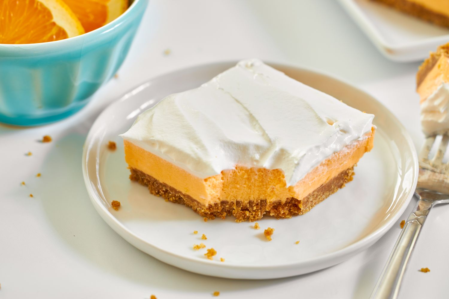 A creamsicle dessert bar with a graham cracker crust topped with whipped cream on a plate