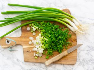 Overhead shot of a bunch of scallions, part of them chopped up, on a wooden cutting board
