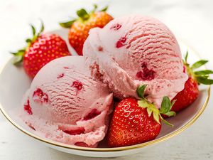 A bowl containing strawberry ice cream scoops and fresh strawberries