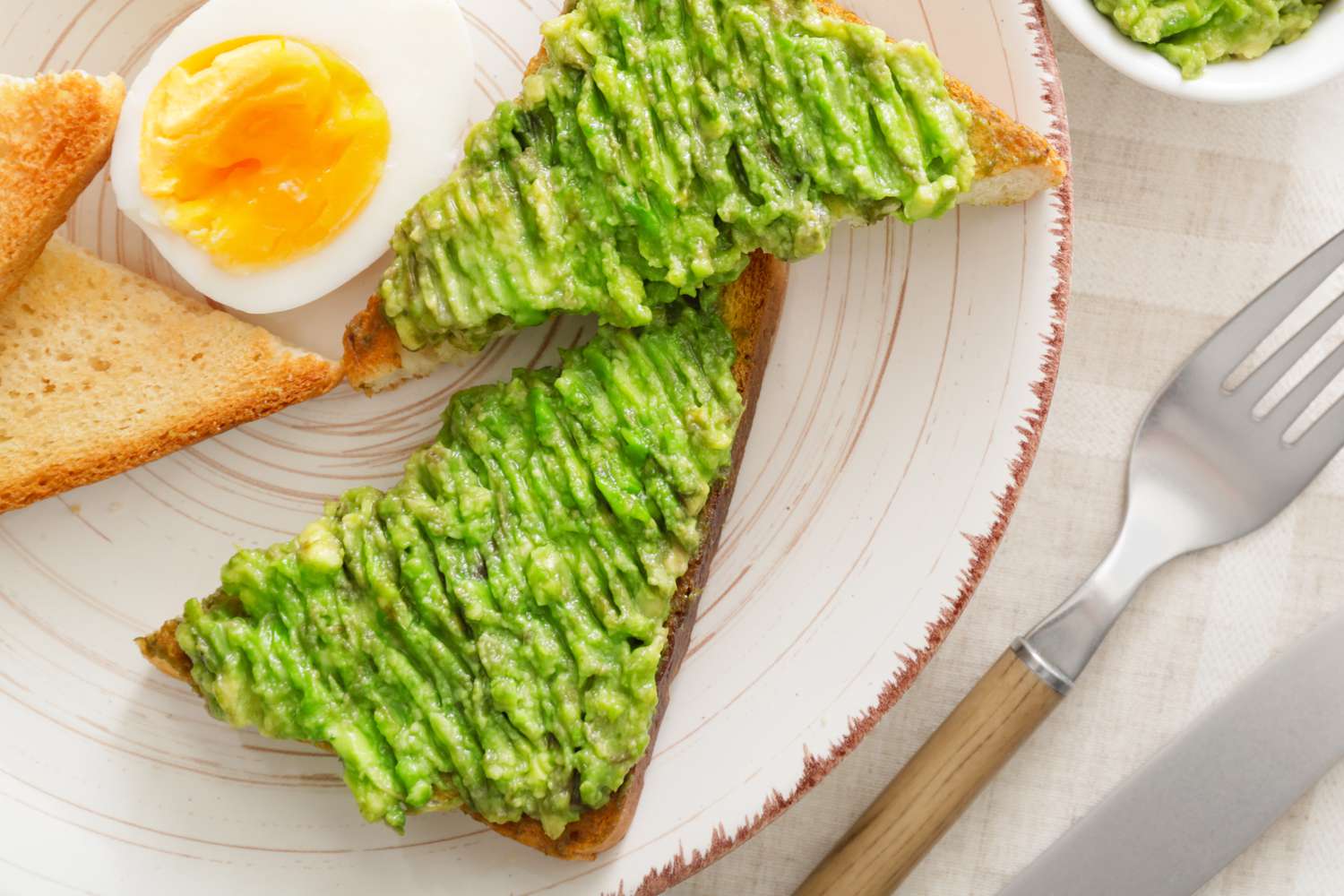Avocado toast and a boiled half egg on a white plate