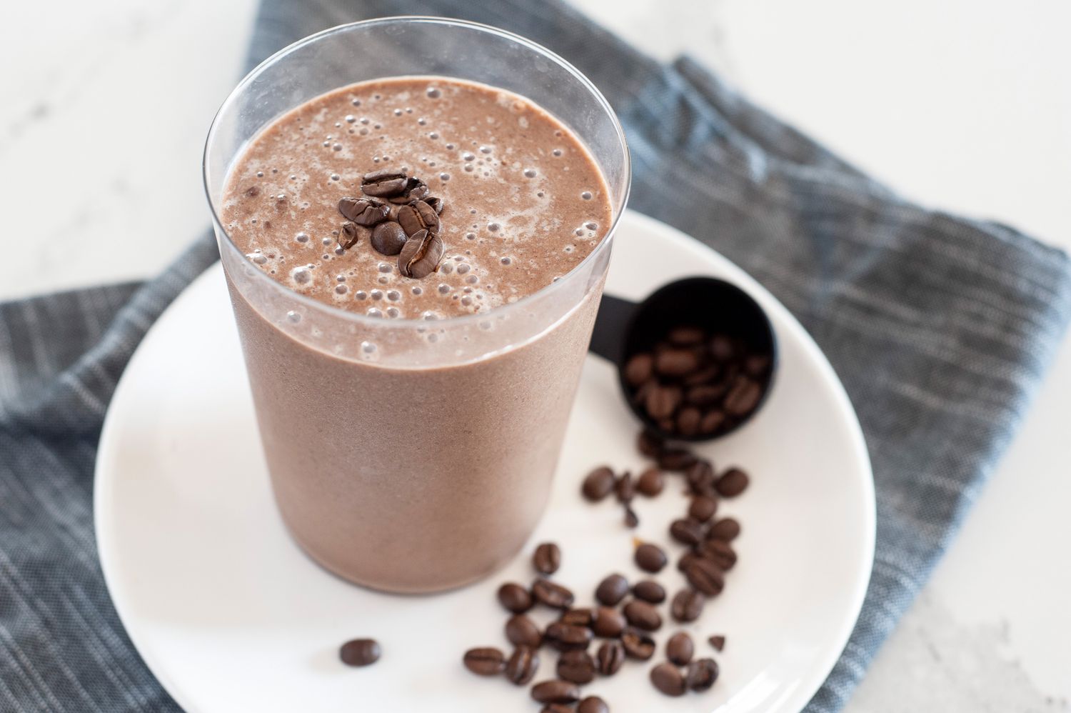 Side view of a coffee banana smoothie on a plate along with coffee beans.