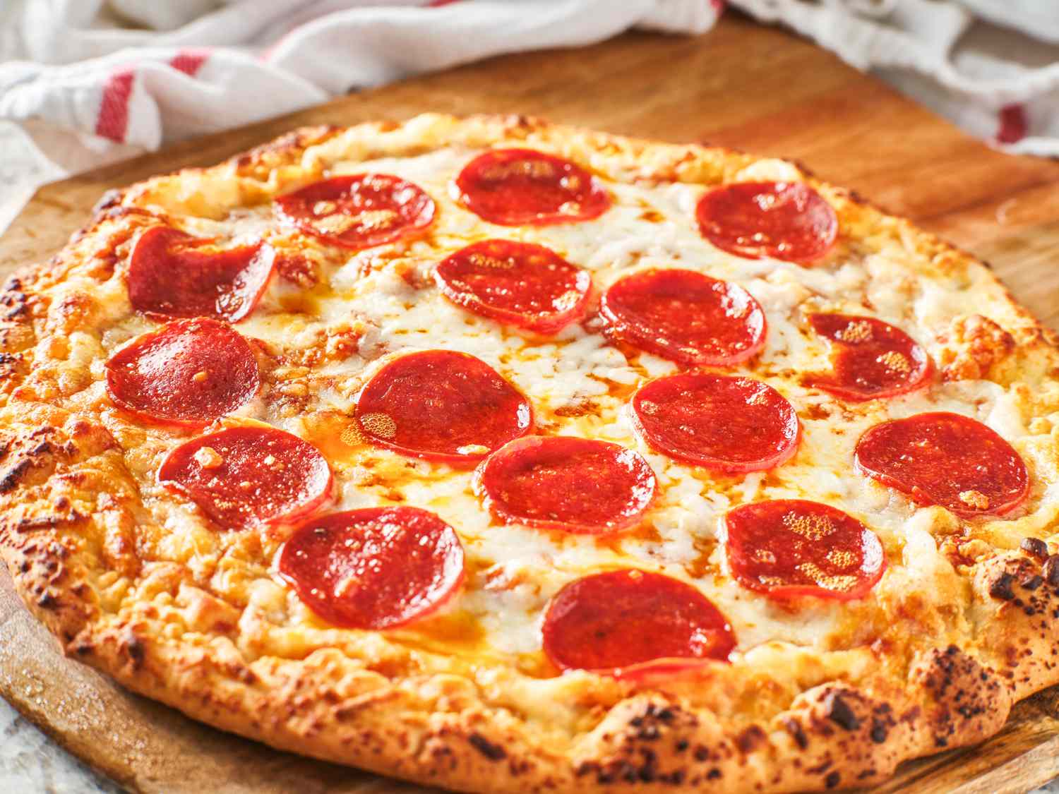 pepperoni pizza on a wooden board surrounded by kitchen towels