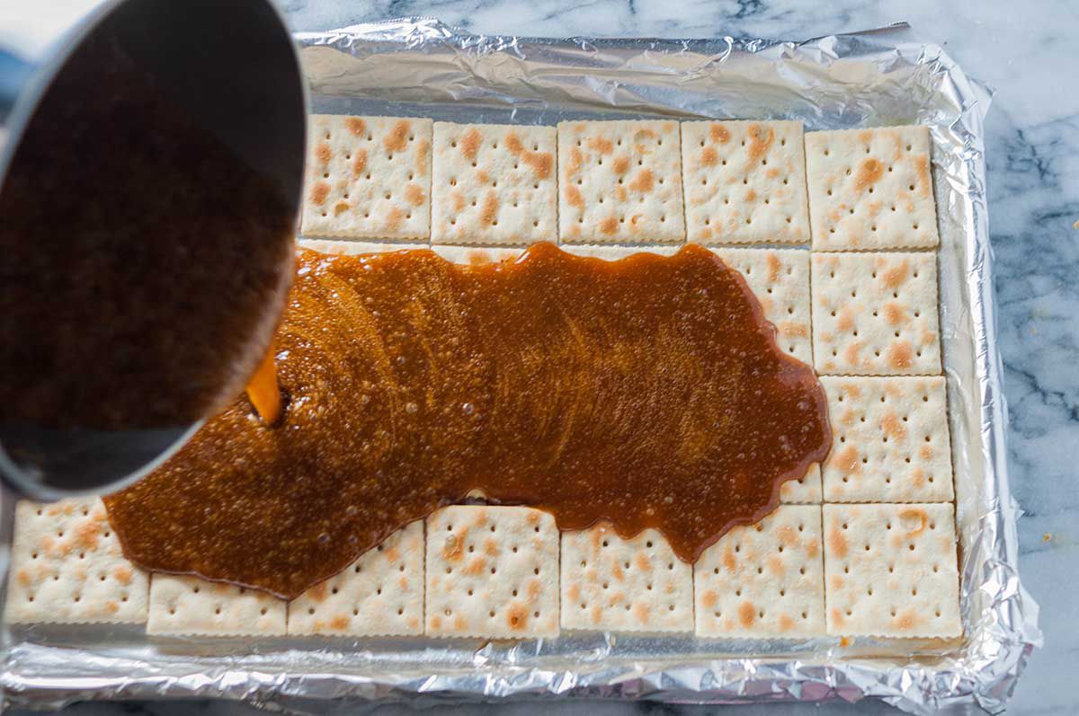 Brown sugar mixture being poured over the saltine crackers in a foiled baking sheet